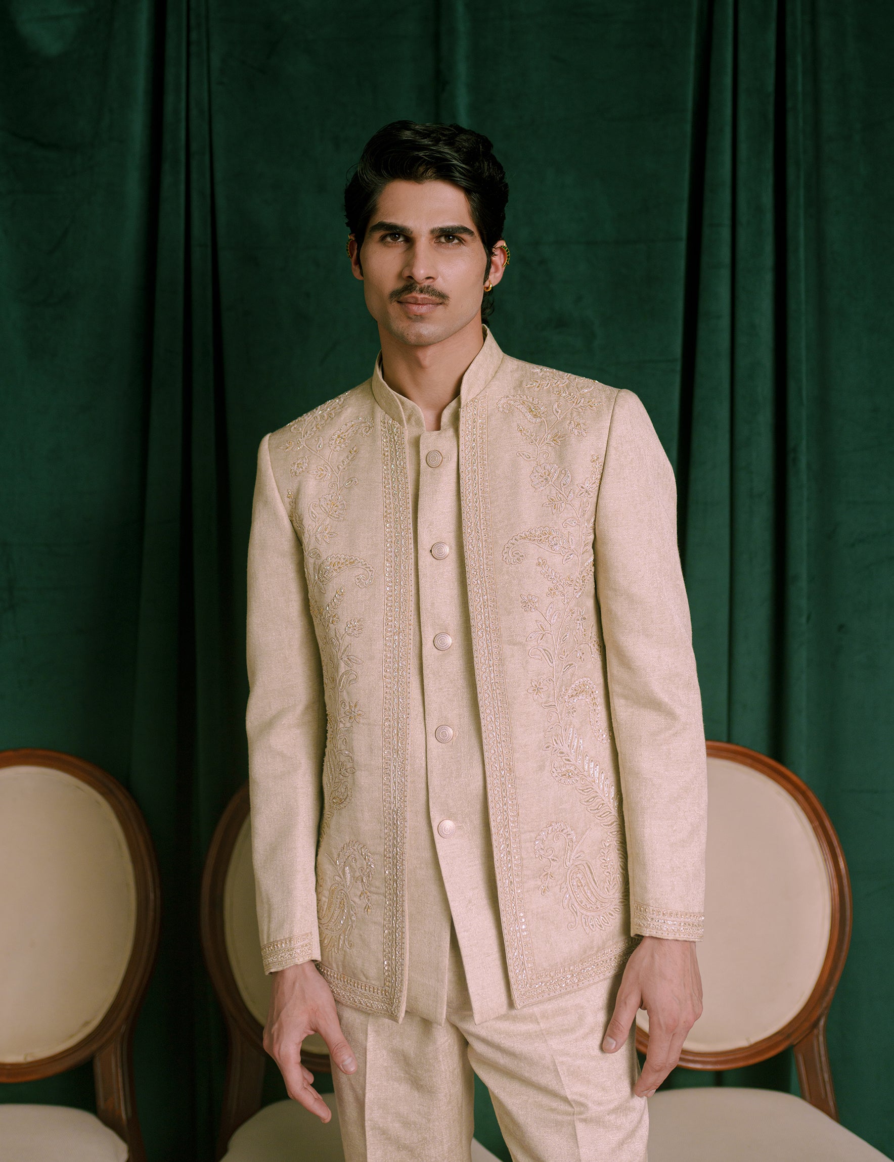 A man wearing a beige-colored embroidered Indian jodhpuri and matching trousers.