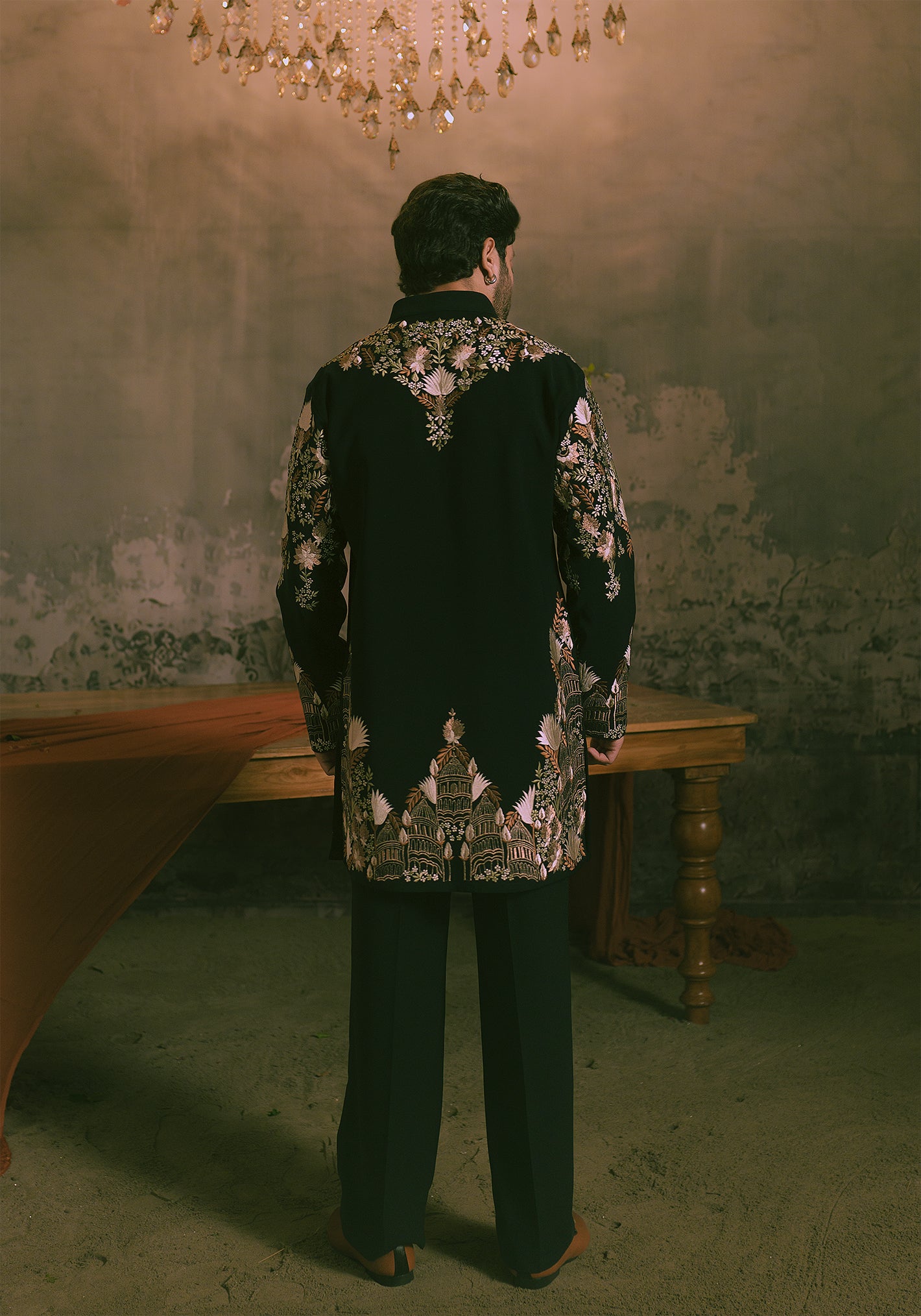 A man viewed from behind wearing a black embroidered short kurta with intricate embroidery.