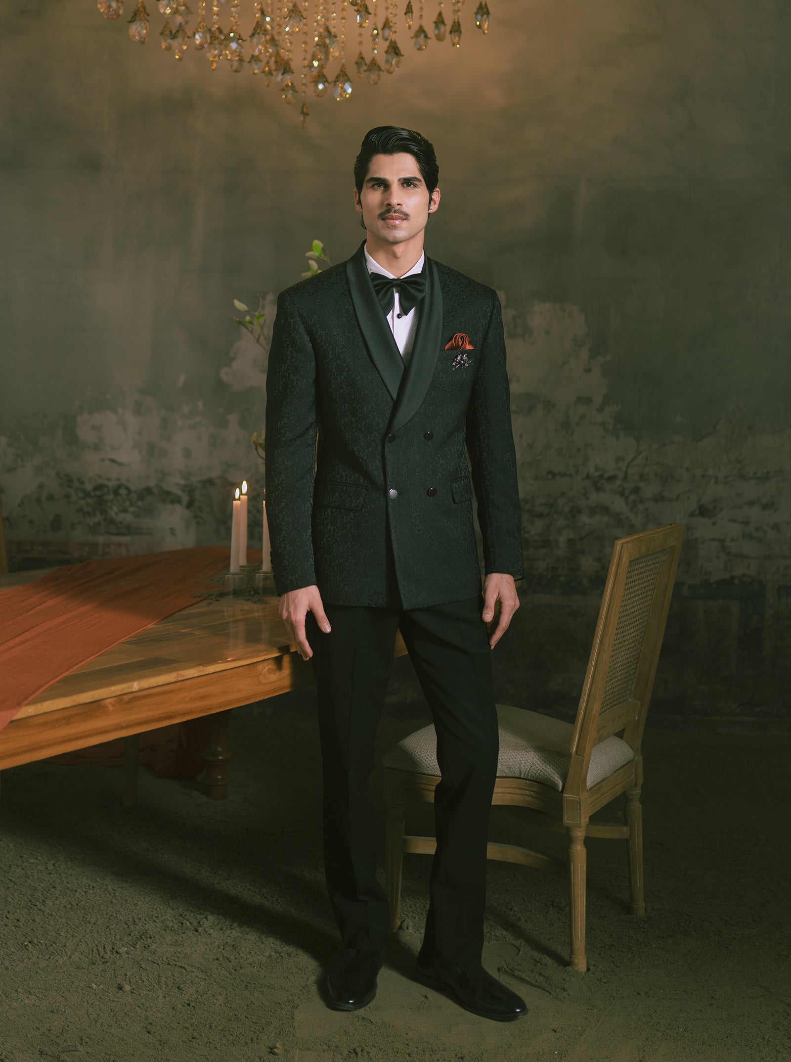 This man is wearing a black double-breasted tuxedo with a black bow tie and pocket square.