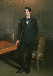 A man wearing a dark double-breasted suit with a subtle pattern, a white shirt, a black bow tie, and a red pocket square.