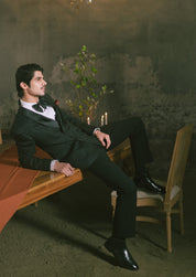 A man in a black tuxedo suit with a white shirt and black bow tie.