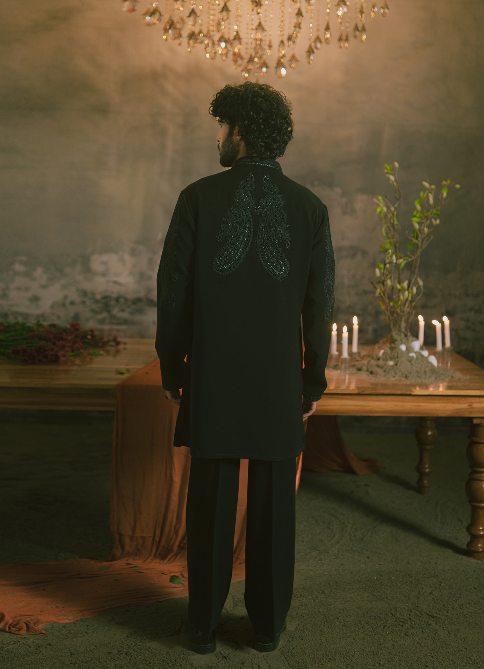 A man viewed from behind wearing a black short kurta with intricate embroidery.