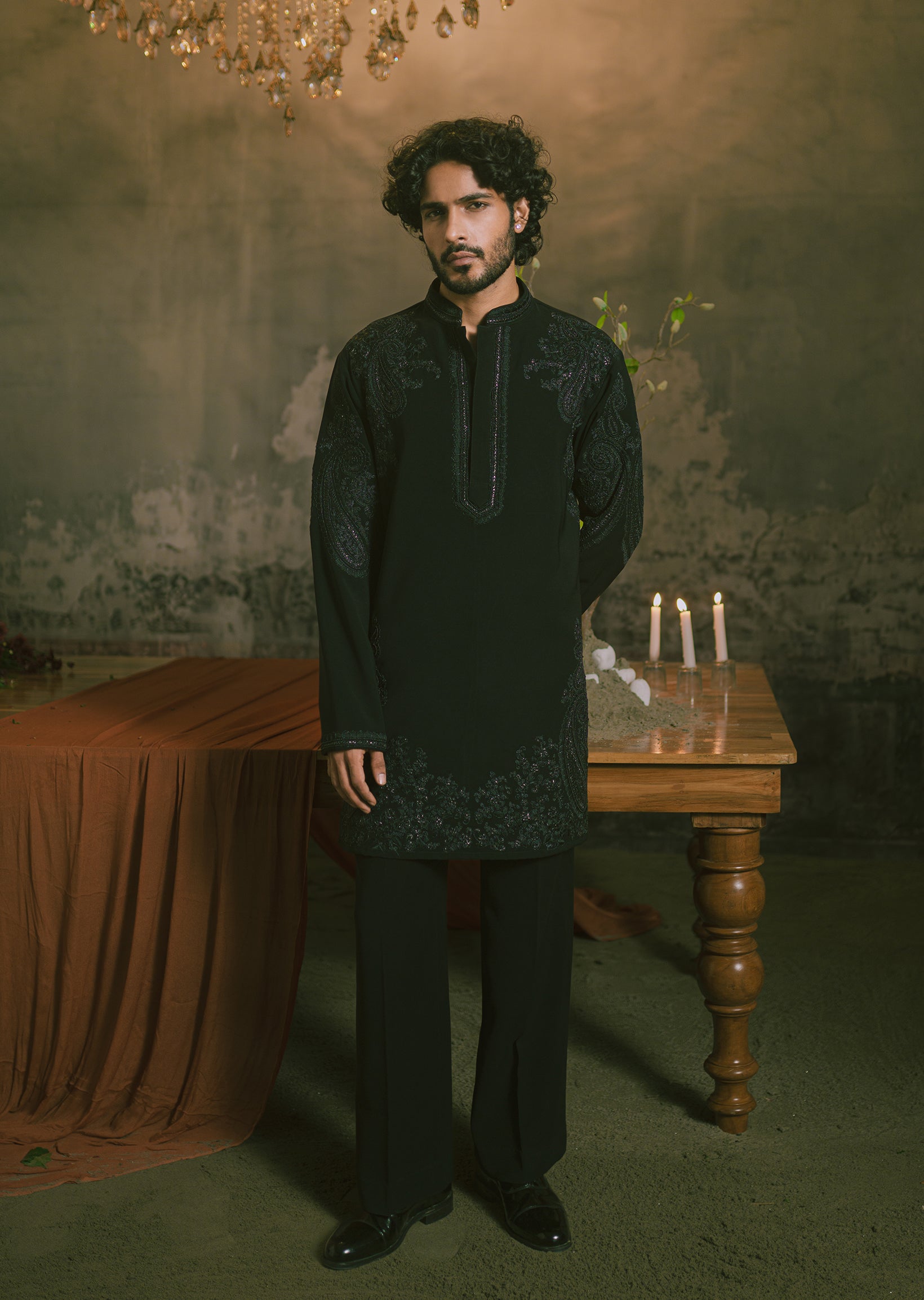 A man wearing a black embroidered short kurta and matching trousers.
