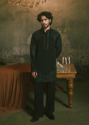 A man wearing a black embroidered short kurta and matching trousers.