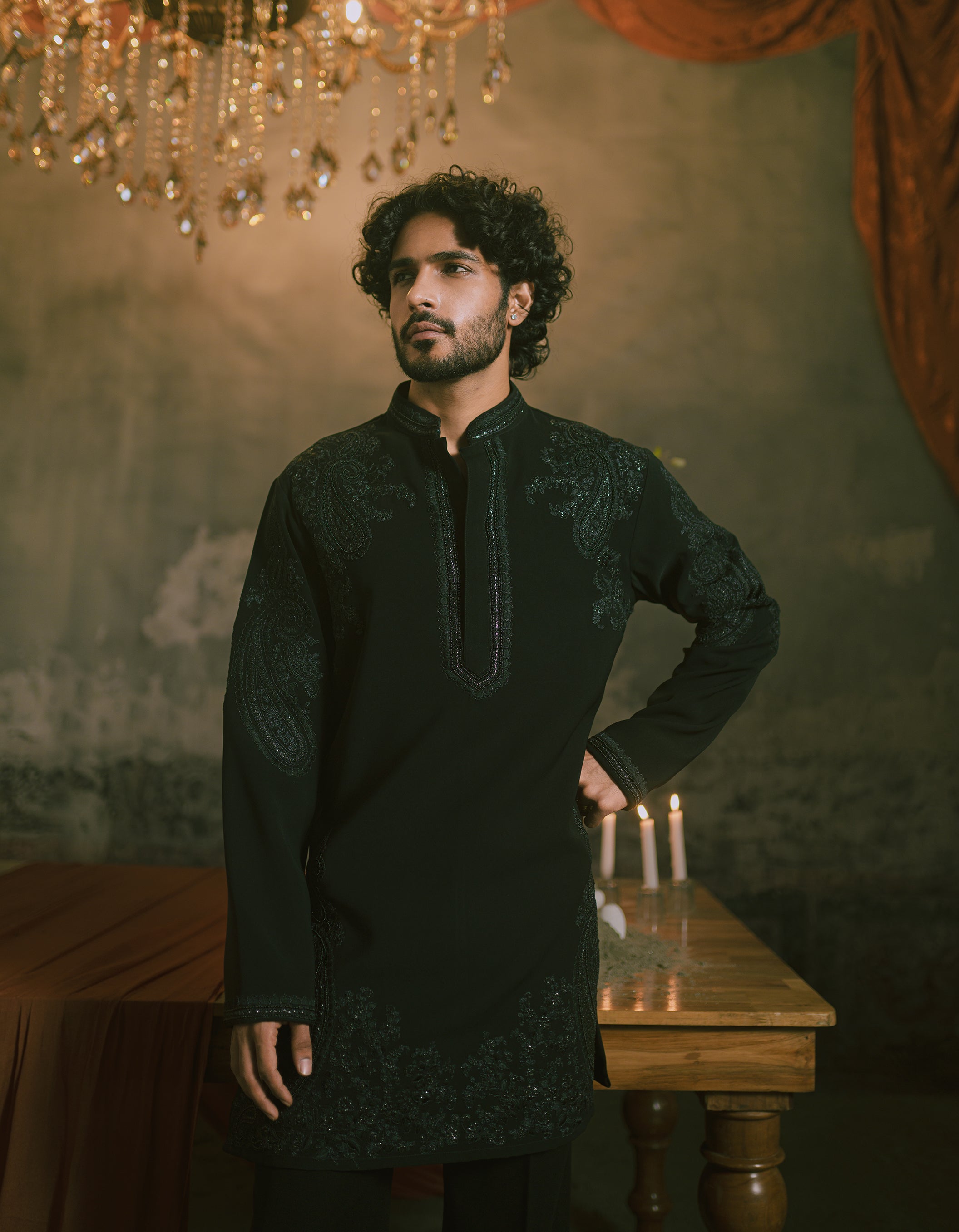 A man wearing a black long-sleeve short kurta with intricate embroidery & wide bottom trousers.