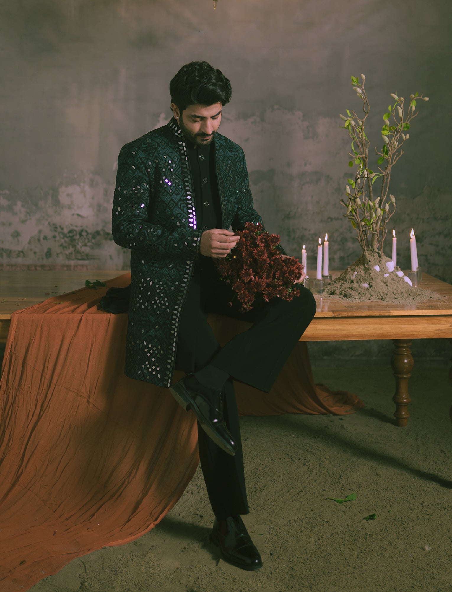 A man is wearing a black embroidered jacket with mirror embellishments, black trousers