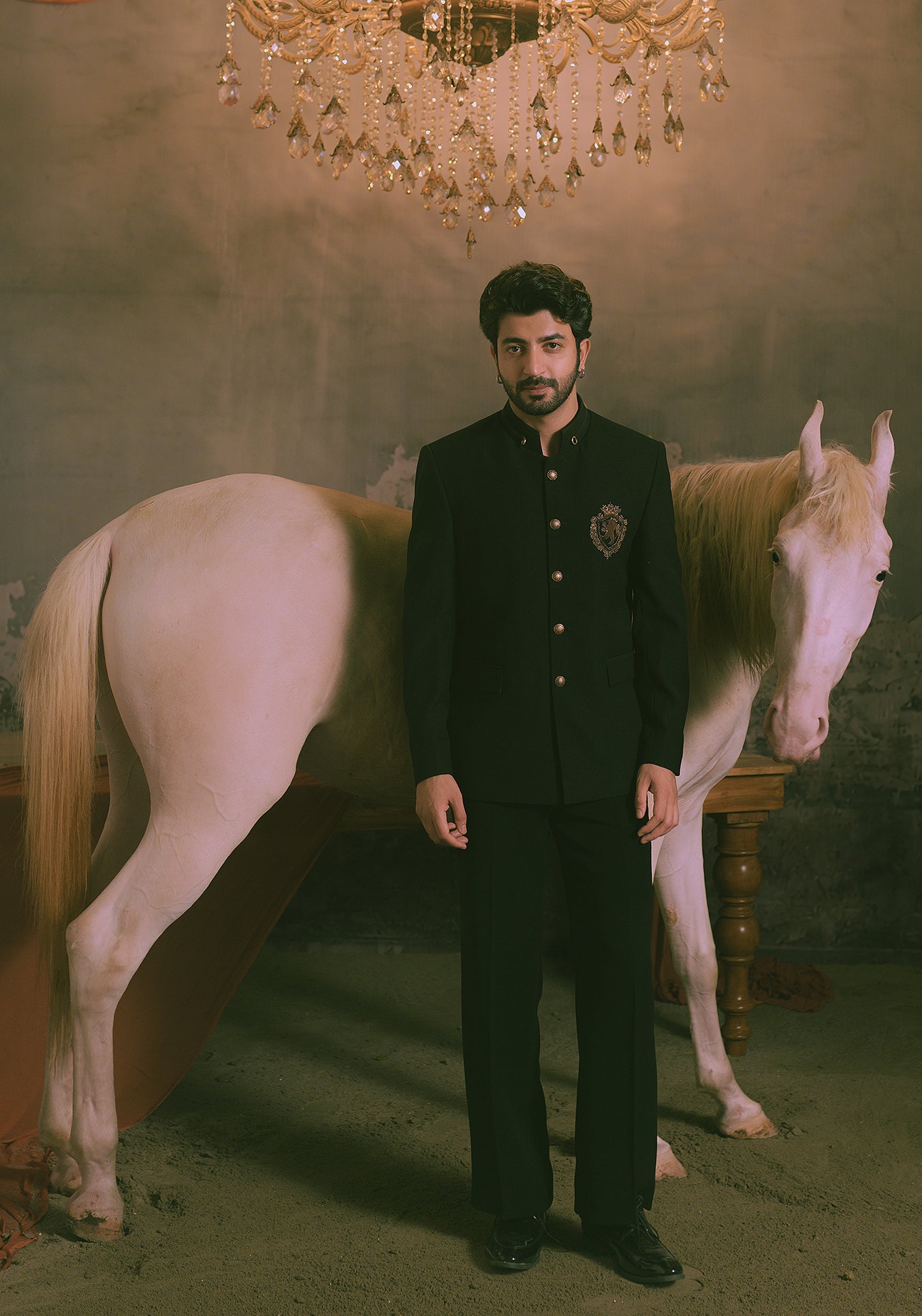 A man in a black traditional formal suit stands in front of a white horse.