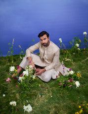 Men's cream Indo-western suit featuring a silk blend top, trousers, and long sleeveless jacket with zari work.