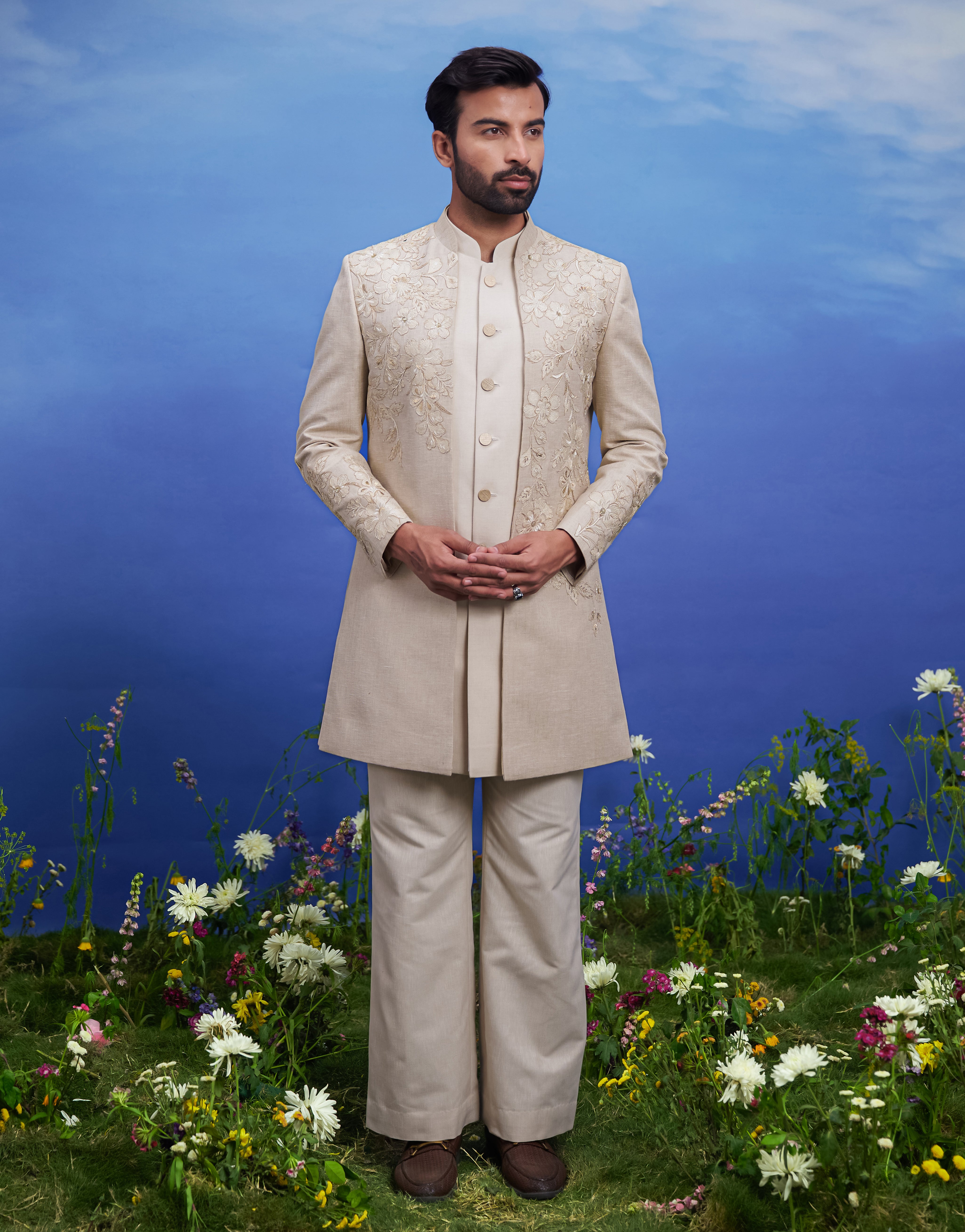 Elegant men's Indo-western outfit with cream floral embroidery and zari, suitable for cultural and celebratory events.