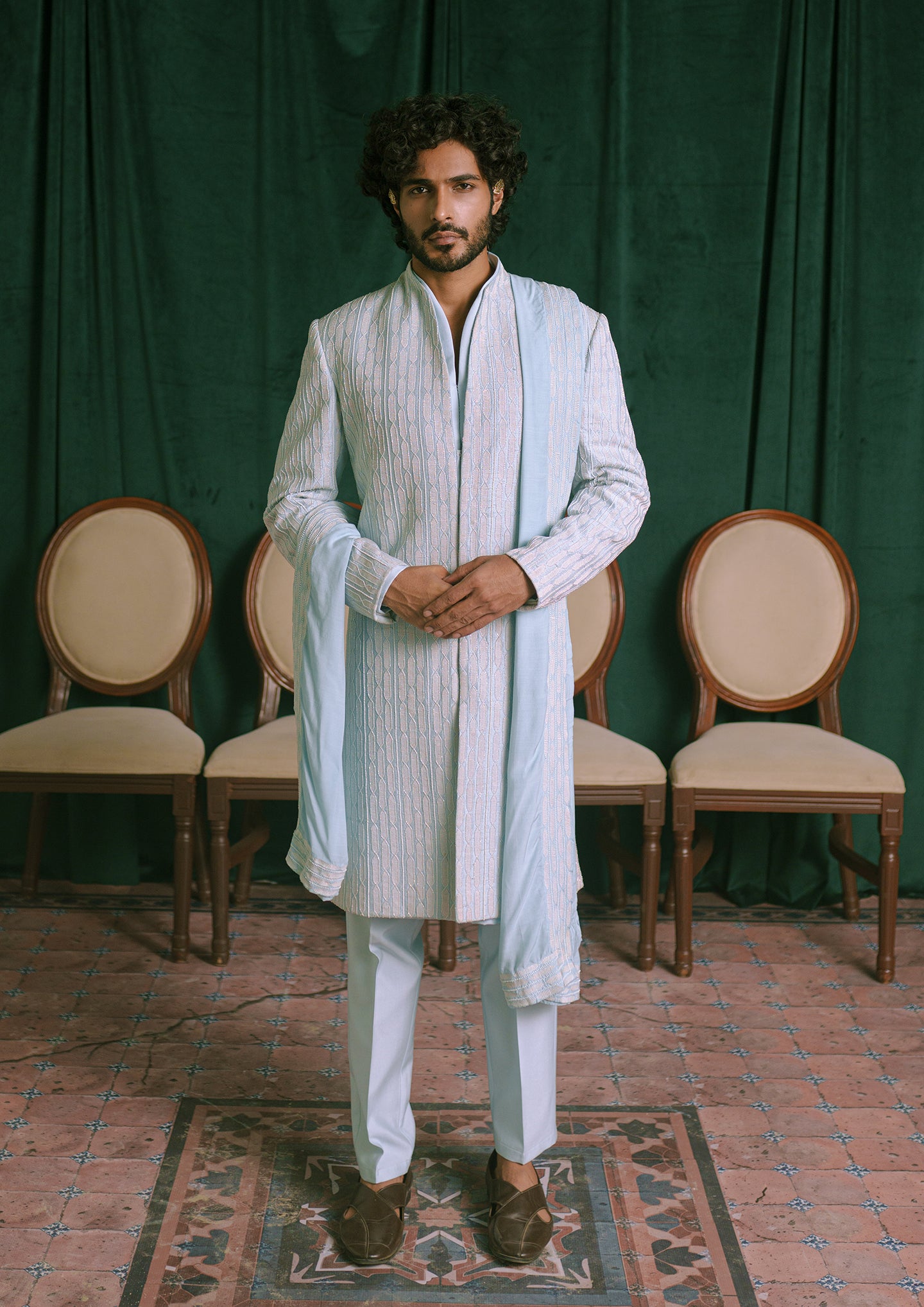 A man is wearing a light blue embroidered sherwani with a matching light blue shawl draped over his shoulders.