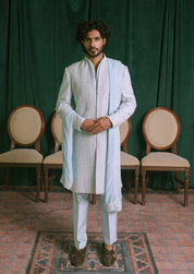 A man is wearing a light blue embroidered sherwani with a matching light blue shawl draped over his shoulders.