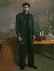 A man is wearing a blue and black heavily embellished with mirror and thread embroidery sherwani jacket over a black indowestern.