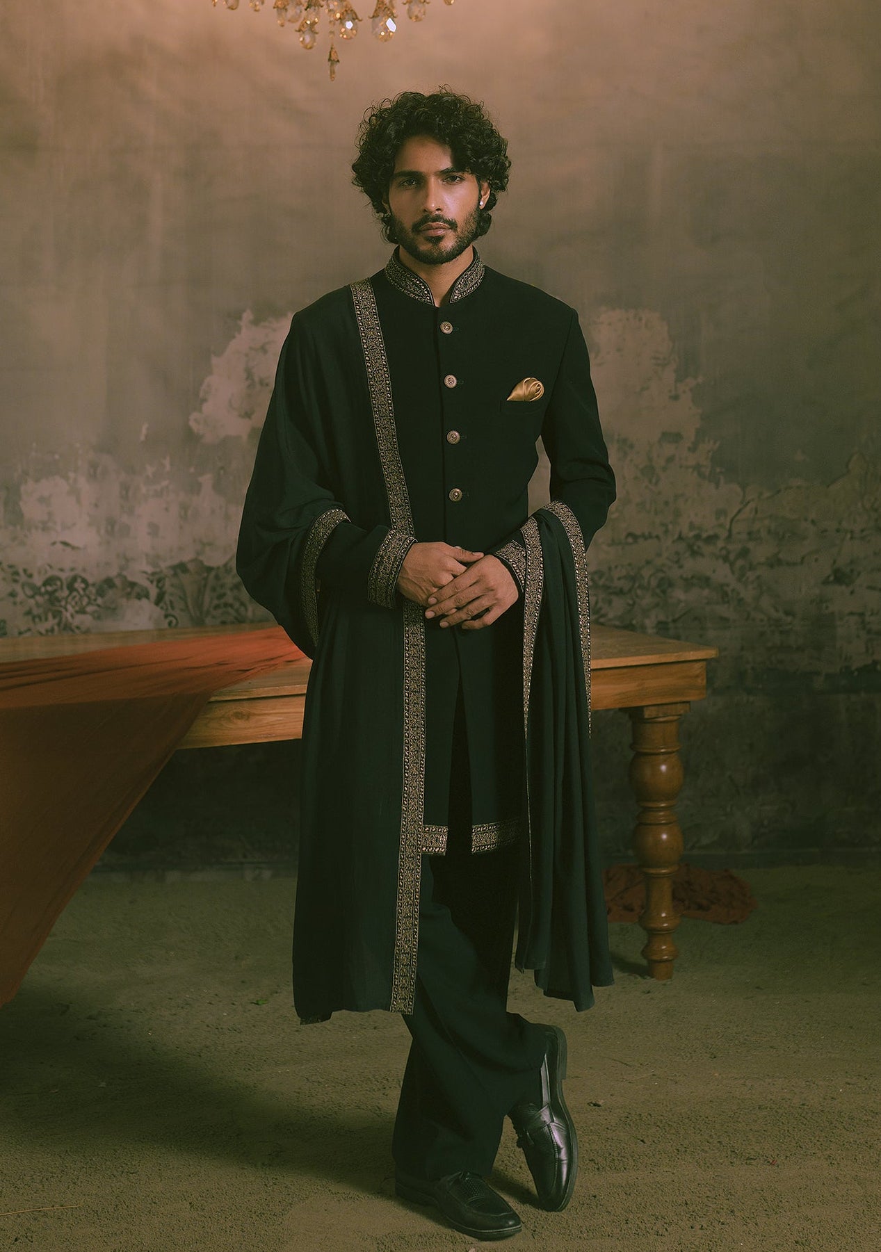 A man wearing a traditional black sherwani with ornate silver-gray border trim and gold buttons.