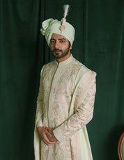 A man is wearing a traditional Indian embroidered Sherwani for groom with a light green turban and a matching embroidered stole.
