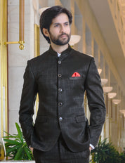 A man wearing a black checkered terry rayon jodhpuri blazer with a five-button placket and three front pockets, standing in a luxurious setting.