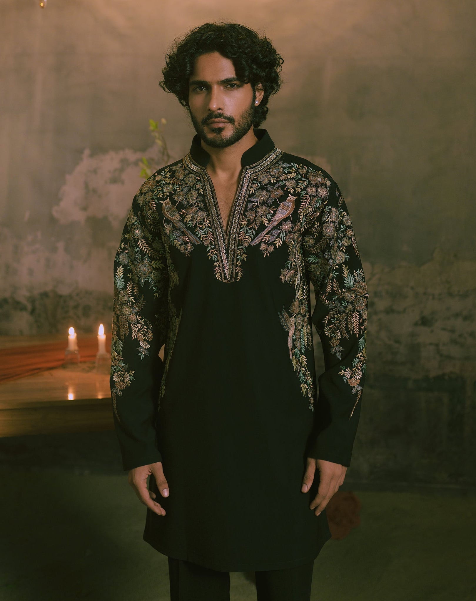 A man wearing a black long-sleeve kurta with ornate multicolor floral embroidery on the chest and sleevesl.