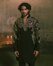 A man wearing a black long-sleeve kurta with ornate multicolor floral embroidery on the chest and sleevesl.