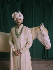A man wearing a traditional pink sherwani with gold embroidery.